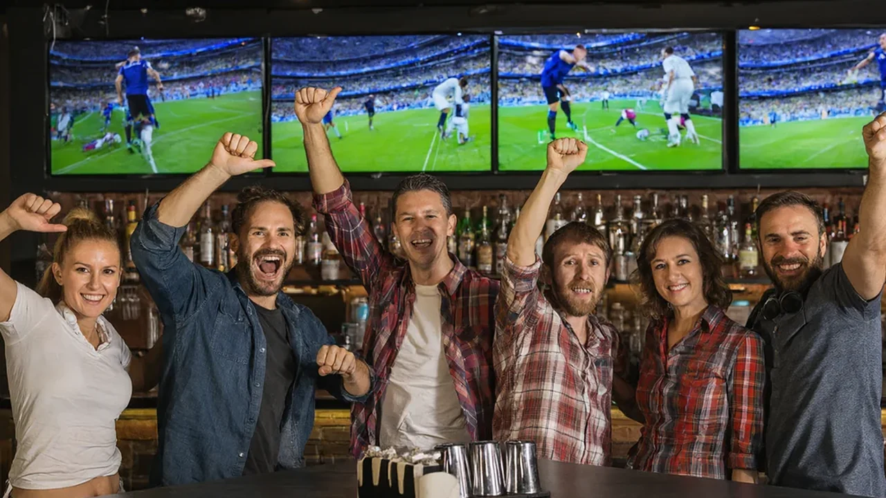 Group of friends in a New York sports bar cheering a Champions League goal on a wall of screens