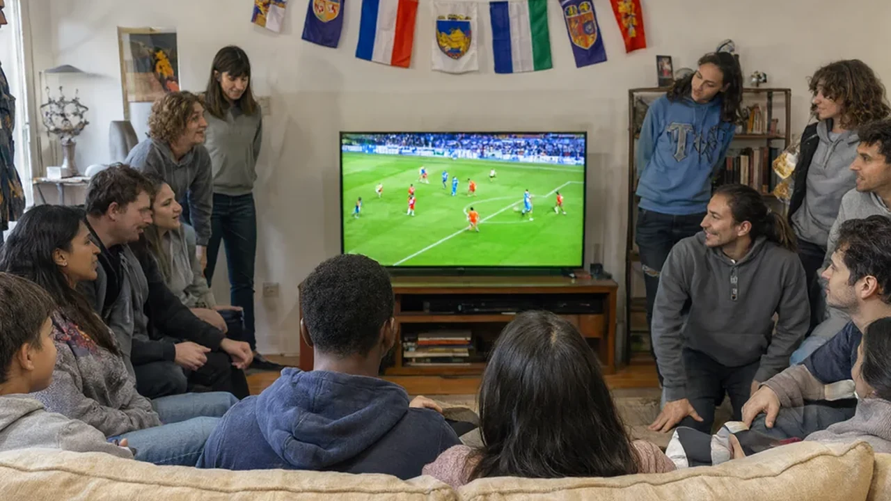 American family and friends around a television in a living room decorated with USA flags